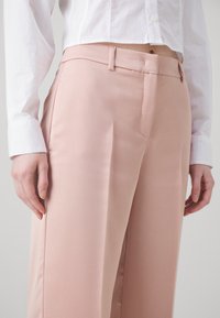 Lichtroze broek van gladde stof, slim fit met zijzakken en persplooien, gecombineerd met een witte blouse met kraag.