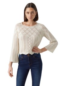Maglione bianco a maglia, taglio cropped, con un design a motivo e maniche a tre quarti, abbinato a jeans in denim blu scuro.