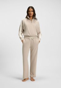 Beige rits-sweatshirt met een hoge kraag en een losse pasvorm, gecombineerd met bijpassende joggingsbroek met een elastische tailleband en trekkoord.