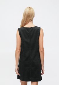 Čierne rifľové šaty bez rukávov s okrúhlym výstrihom, jednoduchým dizajnom a viditeľným prešitím pozdĺž zadného švu a lemu.