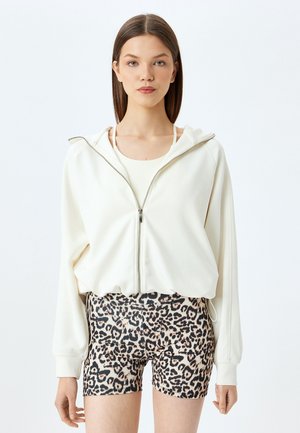 Creme kleurige rits hoodie met een losse pasvorm en kangoeroe zakken, gecombineerd met strakke shorts met luipaardprint met een zachte textuur en een elastische tailleband.