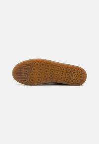 Suela de zapato de goma con una superficie texturizada, que presenta patrones circulares y surcos horizontales. El color es marrón con un acabado ligero y granuloso.