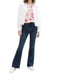 Chemisette blanche par-dessus un haut à motifs rose et blanc, associée à un jean évasé bleu foncé et des baskets blanches.