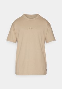 Bežové bavlněné tričko s krátkým rukávem, žebrovaným kulatým výstřihem a malým vyšívaným logem Nike na hrudi. Jednoduchý, rovný střih.