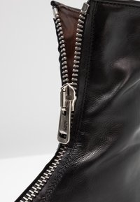 Bota de cuero negra con un detalle de cremallera plateada a lo largo del costado. Textura suave con un diseño elegante, que muestra costuras precisas.
