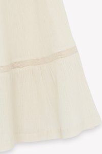 Cream-colored skirt featuring a textured fabric with a flared hemline, accented by a narrow open weave strip near the bottom.