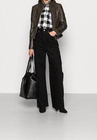 Czarna skórzana kurtka, czarna i biała koszula w kratę, wysokie czarne spodnie, czarna torba na ramię i czarne botki za kostkę. Gładka tekstura, dopasowany krój.