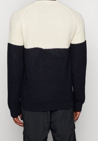 Pull en maille bleu marine et crème avec un motif texturé et des poignets côtelés. Design contrasté avec un bloc de couleur horizontale sur le haut du dos.