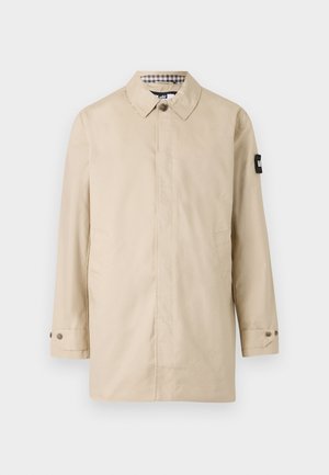 Cappotto leggero beige con taglio dritto, colletto abbottonato, tasche laterali e un accento nero sulla manica sinistra. Foderato con motivo a scacchi.