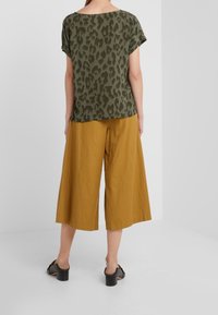 Blusa de estampado de leopardo en verde oliva, de corte relajado, combinada con pantalones anchos color mostaza. Tejido suave y sandalias de tacón grueso a la altura del tobillo.