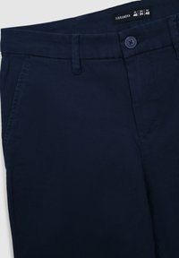 Pantaloni in cotone blu navy con una texture liscia, dotati di chiusura con bottone, passanti per la cintura e tasche laterali. Etichetta del marchio visibile in vita.