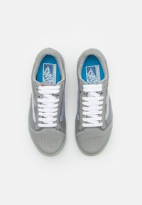 Ténis cinzentos com uma superfície texturizada e painéis de malha. Apresentam cordões brancos, uma palmilha azul e uma sola de borracha transparente.