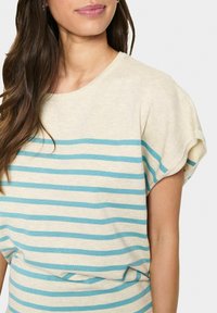 Camisa de manga corta a rayas en color crema con rayas horizontales en turquesa y beige. Tejido suave, corte relajado y escote redondo.