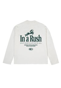 Camisa blanca de manga larga con gráfico de caballo verde oscuro y texto "In a Rush INTERNATIONAL", "Modern Yuppies Worldwide" y "Berlin Avantgarde" en la parte trasera.