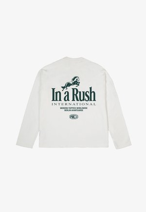 Chemise blanche à manches longues avec un graphisme de cheval vert foncé et les textes "In a Rush INTERNATIONAL", "Modern Yuppies Worldwide" et "Berlin Avantgarde" au dos.