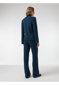 Conjunto de suéter y pantalones en azul oscuro, fabricado con un tejido suave, que presenta un corte relajado, mangas largas y bajos de pantalón ligeramente acampanados.