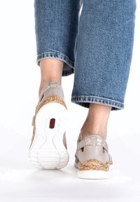 Hellgraue Schuhe mit strukturiertem Finish und korkähnlichen Akzenten, ausgestattet mit einem Riemen hinten und einer Gummisohle, kombiniert mit blauen Jeans.