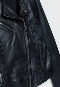 Giubbotto biker in pelle nera con cerniere argentate, numerose tasche con zip e colletto a punta. Texture liscia, design aderente.