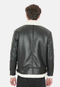 Giubbotto in pelle nera con collare in shearling, finitura testurizzata e fibbia regolabile in vita, che mette in mostra un design semplice e strutturato.