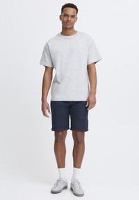 Szary bawełniany T-shirt z krótkim rękawem, zestawiony z granatowymi szortami z podwiniętymi mankietami oraz jasnoszarymi trampkami z białymi akcentami.