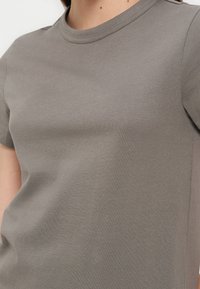 Κοντινή λήψη ενός ατόμου που φοράει μια απλή κοντομάνικη βαμβακερή μπλούζα σε χρώμα ταουπ με στρογγυλή λαιμόκοψη και λεία υφή υφάσματος.