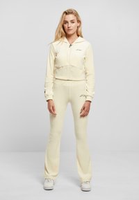 Haut zippé jaune avec un design court et un logo brodé, associé à un pantalon évasé assorti. Complété par des baskets blanches.