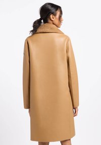 Tanleren jas met een zachte bruine bontkraag, ontwerp tot de knie, rechte silhouet en minimale naden voor een strakke uitstraling.