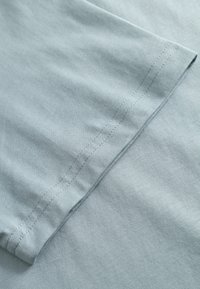 Tissu bleu clair à texture lisse, avec un ourlet replié et un détail discret de couture. Le matériau semble doux et léger.