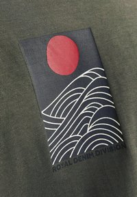 Olive green fabric with a navy rectangle patch featuring a red circle and white wave pattern, accompanied by the text "ROYAL DENIM DIVISION."