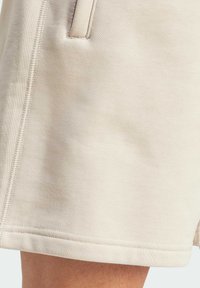 Beige sportshorts tillverkade av mjukt material. Har en rak fåll, sidofickor och synliga sömmar längs sömmarna.