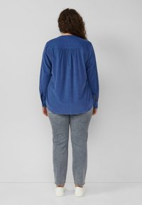 Blaues Langarmhemd mit einem Rückenpasse-Design und geknöpften Manschetten, getragen mit grauen geraden Hosen und weißen Schuhen. Glatte Stofftextur.