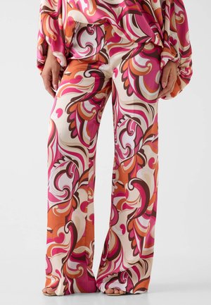 Pantalon ample à jambes larges avec des motifs tourbillonnants audacieux en rose, orange, blanc et marron, associé à un haut à manches longues assorti et des sandales ouvertes.