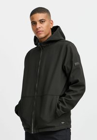 Veste zippée noire avec capuche, fabriquée en tissu lisse et durable. Elle dispose de poches latérales et d'un petit patch logo sur la manche.