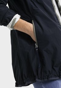 Granatowa, lekka kurtka z zamkiem błyskawicznym z przodu, elastycznym dołem i bocznymi kieszeniami. Posiada białą podszewkę z szarymi akcentami.