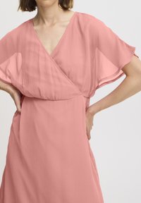 Robe en chiffon rose avec un décolleté en V et des manches flottantes. Le tissu est léger et fluide, avec une taille cintrée.