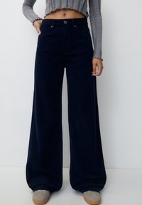 Pantalons en velours côtelé bleu foncé à jambes larges, avec une taille haute, fermeture à bouton, poches avant et une texture douce.