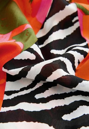 Tessuto colorato caratterizzato da un audace motivo a strisce zebrate in bianco e nero, combinato con forme floreali vivaci in rosa, arancione e verde.