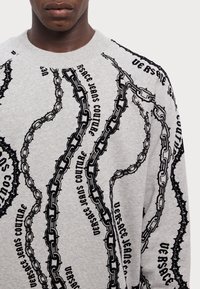 Felpa grigia con un design di catena nera e lettering "VERSACE JEANS COUTURE", texturata con stampa in rilievo e scollo a girocollo.