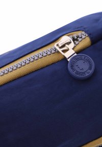 Funda de tela azul marino con un acento dorado, que presenta un cierre plateado y una etiqueta circular azul embellecida con "Caronte Travel & Adventure."