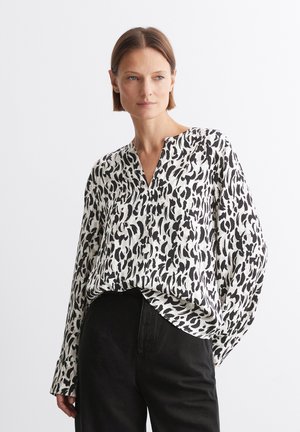 Langärmlige Bluse aus leichtem Stoff mit weißem Grund und schwarzem abstrakten Muster. Verfügt über ein V-Ausschnitt-Design und eine lockere Passform. Kombiniert mit schwarzen Hosen.