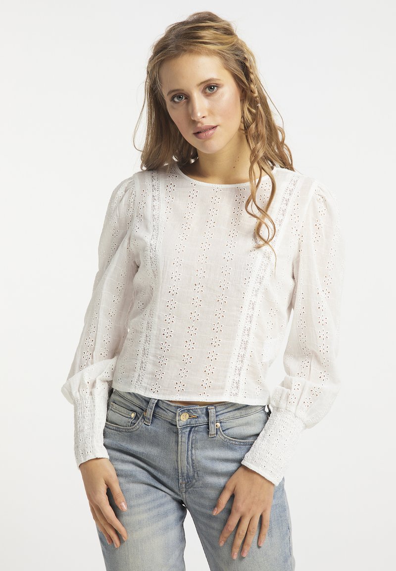 Hvid bomuldsbluse med blomsterbroderi, lange puffærmer og smockede manchetter. Bæres med lyseblå denim-jeans.