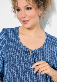 Bluse mit blauem Muster, kurzen Puffärmeln, einem runden Halsausschnitt mit Bindeband und einer strukturierten Stoffgestaltung.