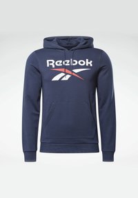 Marineblå hettegenser med frontlomme, snøring i hetten, og stor hvit Reebok-logo med røde detaljer. Glatt stoff med ribbestrikkede mansjetter.