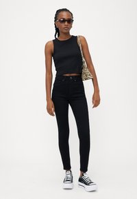Fekete cropped tank top, magas derekú fekete farmernadrág és fekete platform sportcipő. Kiegészítve egy kis zebra mintás táskával.