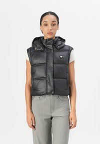 Zwarte gewatteerde vest met capuchon, textuurafwerking, ritssluiting aan de voorkant en contrasterende logo-embleem. Beschikt over horizontale stiksels en zijzakken.