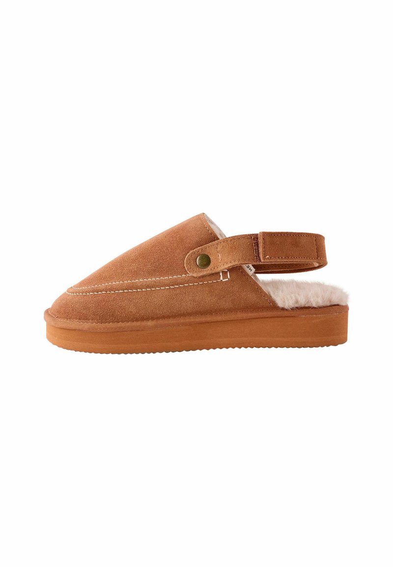 Suedeslipper i brun med en fluffy indvendig foring. Har en flad gummisål og en justerbar rem med en trykknap til tilpasning.