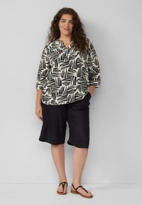 Zwart-wit geblokt blouse met driekwartmouwen, gecombineerd met zwarte shorts en zwarte sandalen met een kleine ronde accent.