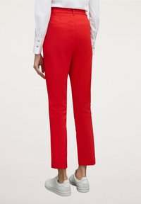 Pantalones rojos hasta el tobillo con textura suave, dos bolsillos traseros y una cintura ajustada, combinados con zapatillas blancas.