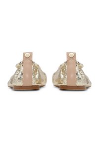Zapatos planos de piel texturizada en tono dorado con detalles en cuero nude en el talón y pequeños botones redondos con el logo dorado, mostrados desde atrás sobre un fondo blanco.