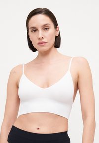 Bralette courte côtelée blanche avec un col en V et des fines bretelles. Texture douce, sous la couture du buste, associée à un bas taille haute noir.